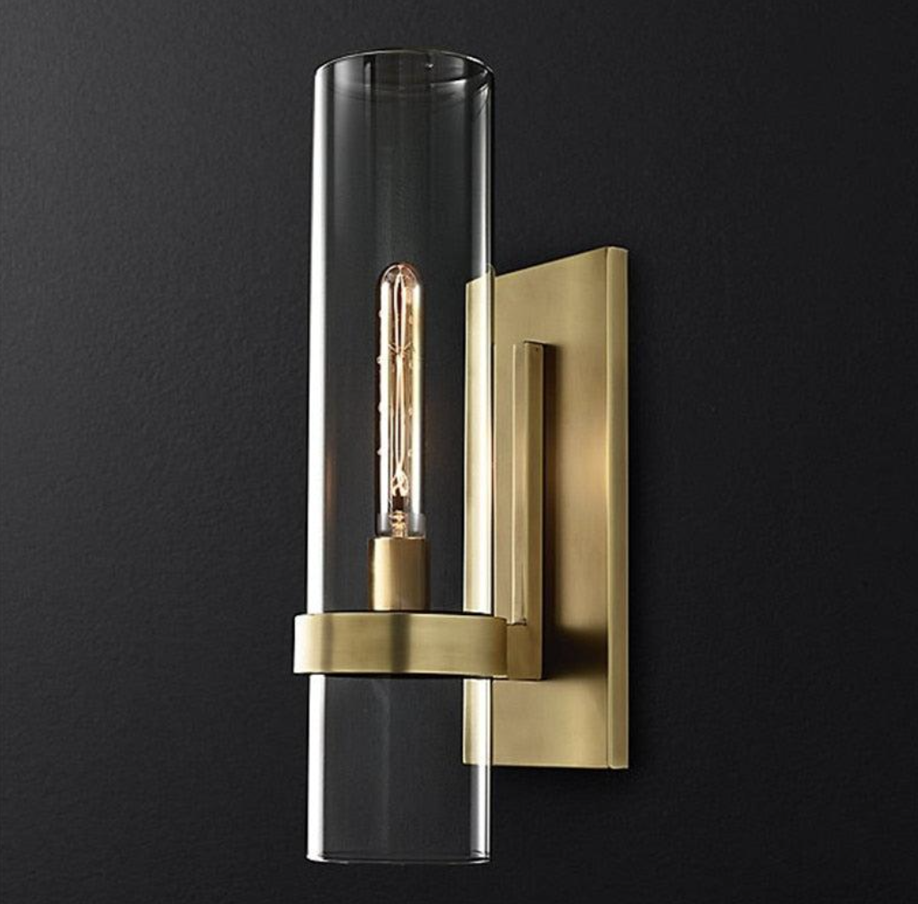 Clear cylindrical glass wall light with a warm metal backplate